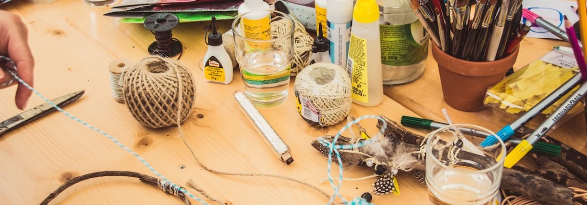 DIY tools on wooden table including thread, glue, and brushes.