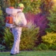 Pest control technician treating a residential yard with a backpack sprayer, outdoor pest control services near St. Louis.