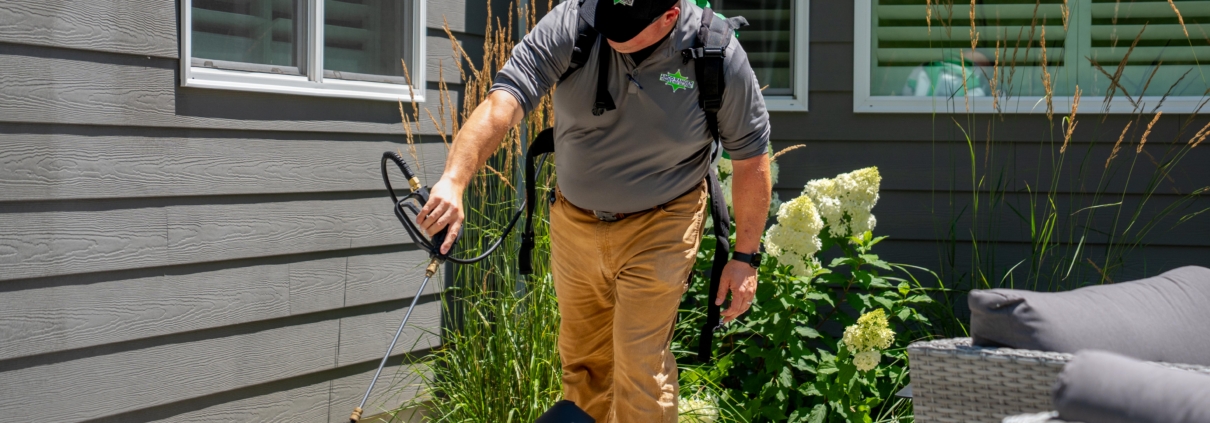 Professional termite and pest control technician from Amco Ranger performing a perimeter liquid treatment on a St. Louis home foundation.