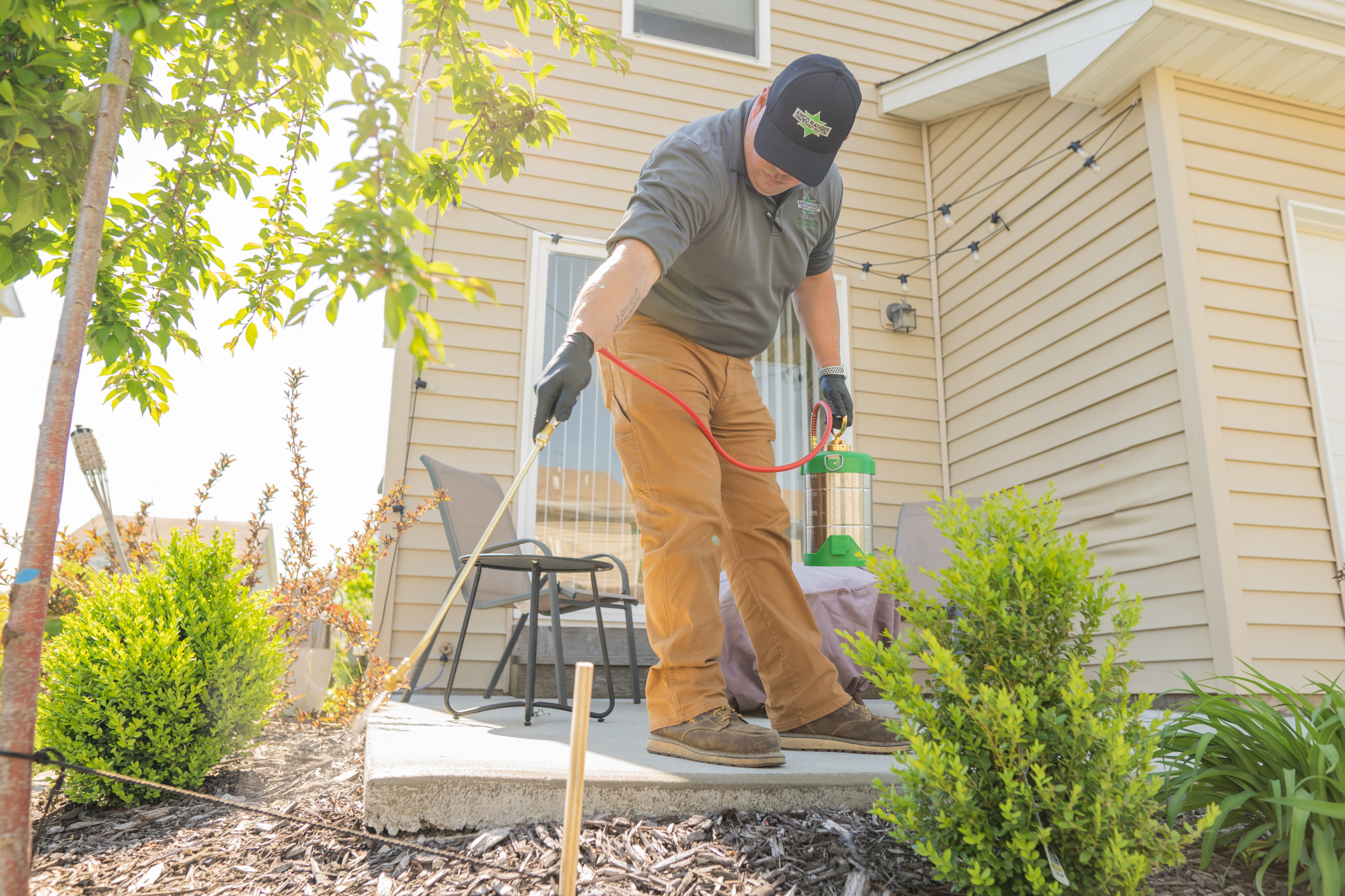 AMCO Ranger technician providing flea control for the yard, spraying mulch beds and shrubs beside a patio
